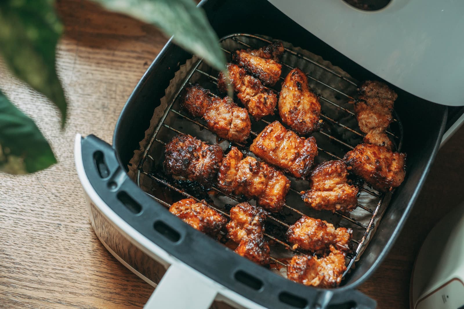 Crispy chicken pieces cooking in a modern countertop air fryer basket on a wood kitchen counter